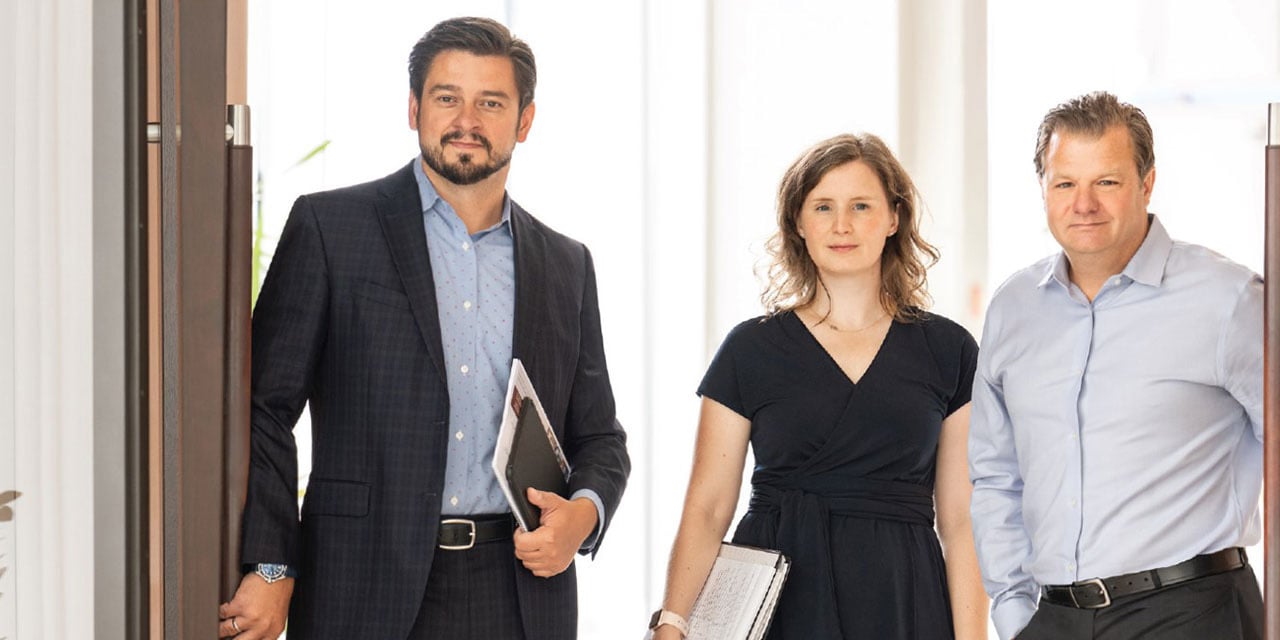 Three professionals walking through a conference room door.