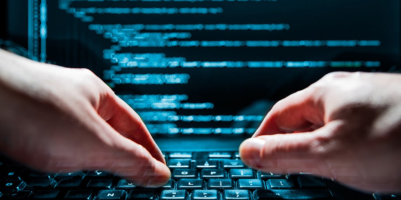 Hands typing on a keyboard with a computer screen in the background.